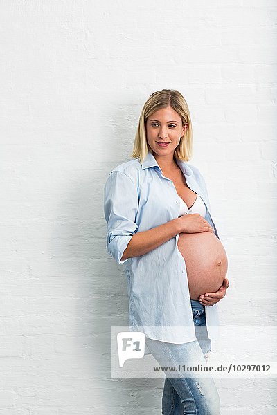 Vollzeitschwangerschaft junge Frau  die sich an die Wand lehnt und den Bauch hält