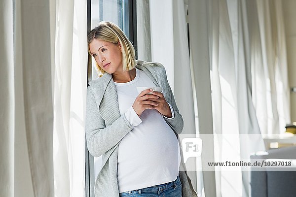Full term pregnancy young woman daydreaming whilst drinking coffee