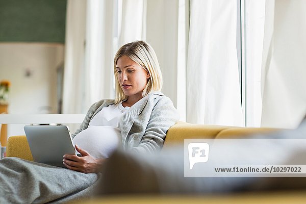 Vollzeitschwangerschaft junge Frau auf Sofa mit digitalem Tablett