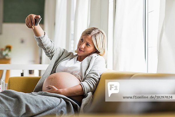 Full term pregnancy young woman on sofa taking selfie