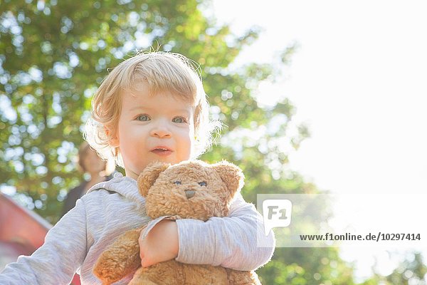 Porträt eines niedlichen weiblichen Kleinkindes mit Teddybär auf der Spielplatzrutsche