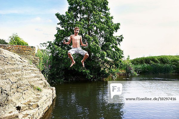 Teenager-Junge springt in der Luft in den See