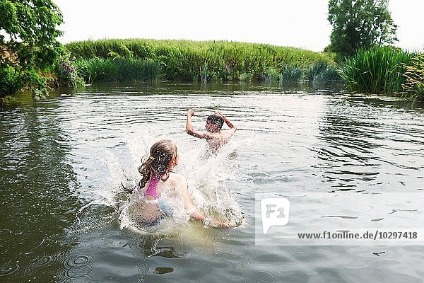 Teenage boy and sister splashing in rural lake