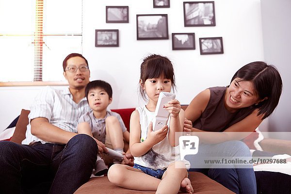 Young  modern Chinese family of parents and two young children sitting on sofa watching television together at home