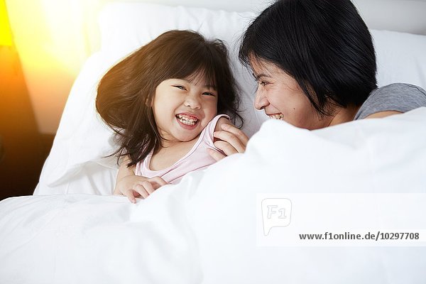 Young Chinese mother and daughter laying in bed together at home