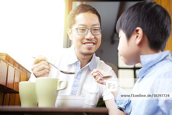Chinesischer Vater und junger Sohn beim gemeinsamen Frühstück auf dem Balkon im Sonnenschein