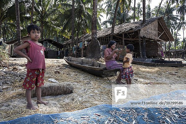 Einheimische Frau und zwei Kinder vor dem Holzhaus eines Fischers unter Palmen am Strand des Fischerdorfes Ngapali  Thandwe  Rakhine-Staat  Myanmar  Asien
