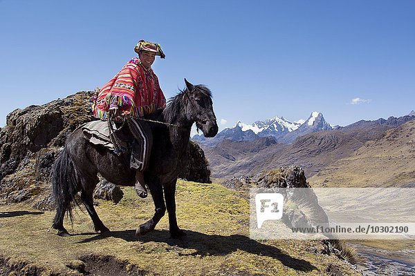 Indio mountain guide with colorful poncho riding on horseback in the mountains Andes Cusco Province Peru South America