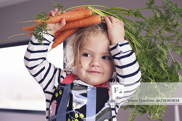 Kleines Mädchen hält frische Karotten über den Kopf  Portrait