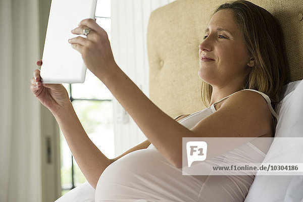 Schwangere Frau mit digitalem Tablett zum Video-Chat mit Freunden und Familie