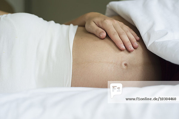 Pregnant woman lying in bed with hand on stomach  cropped