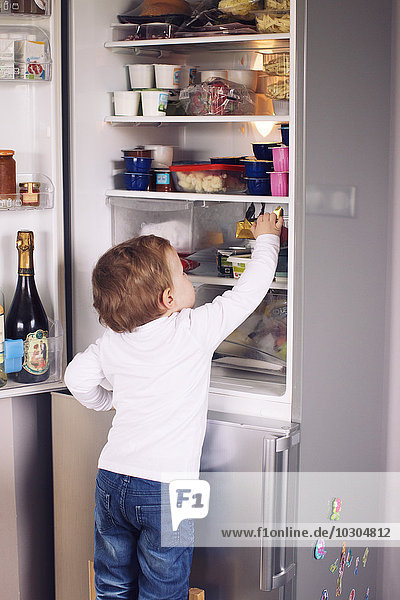 Little boy reaching for something in refrigerator