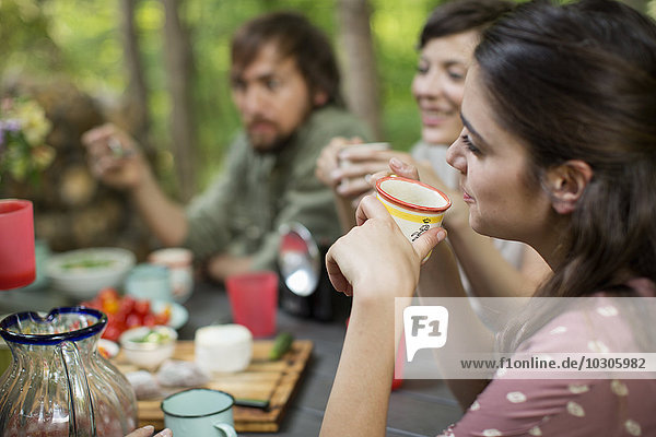 Vier Personen sitzen um einen Holztisch im Wald und teilen sich eine Mahlzeit.