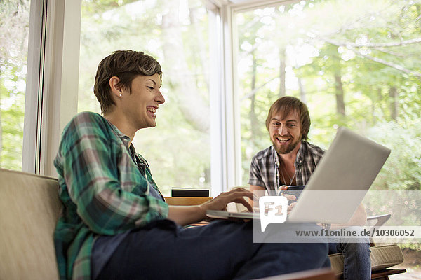Ein Mann und eine Frau sitzen zusammen in einem Raum mit großen Bildfenstern  einer mit einem Laptop.