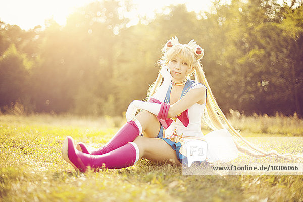 Frau im Kostüm von Pretty Guardian Sailor Moon sitzend auf einer Wiese