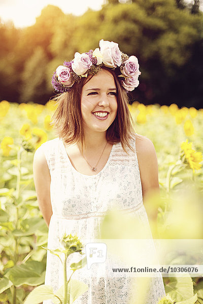 Porträt einer lächelnden jungen Frau mit Blumen auf dem Sonnenblumenfeld