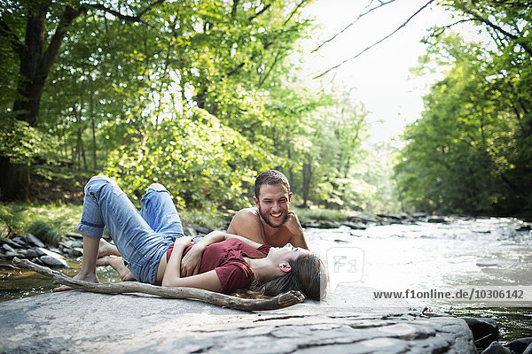 Ein junger Mann und eine junge Frau liegen auf den Felsen an einem Flussufer.