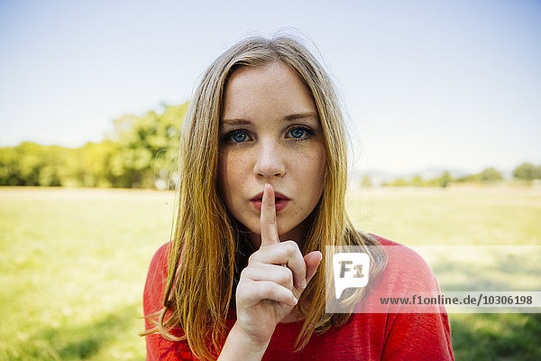 Portrait of teenage girl outdoors putting finger on mouth