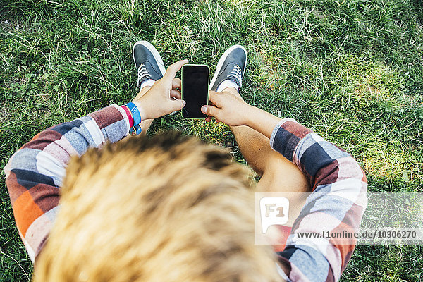 Teenager-Junge sitzt auf der Wiese mit Smartphone
