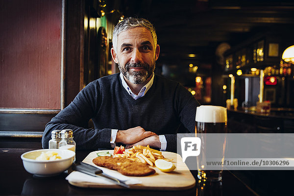 Smiling man in restaurant having Wiener Schnitzel with French fries
