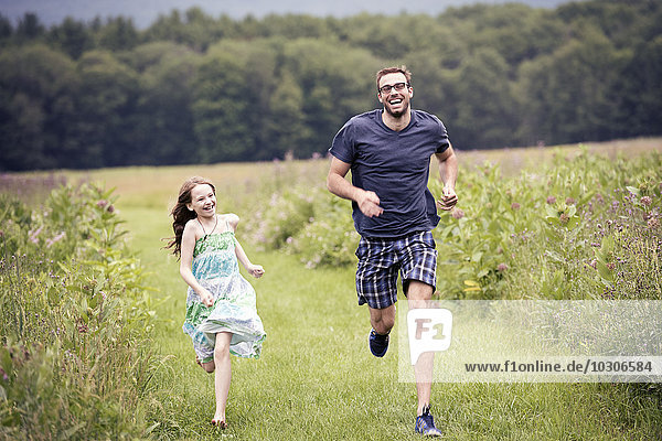 A man and a young child running through a wildflower meadow.