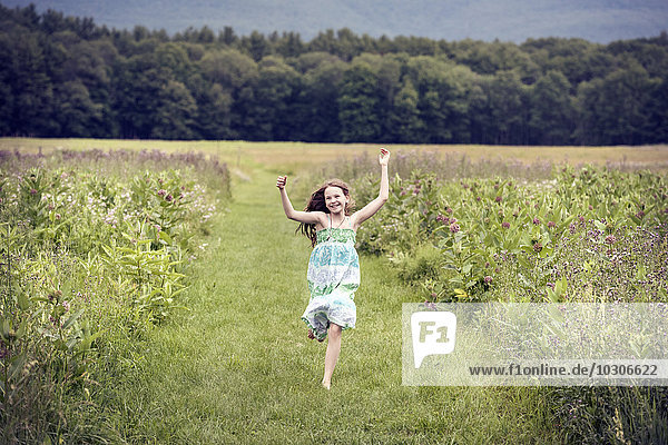 A girl running through a meadow with her arms above her head.