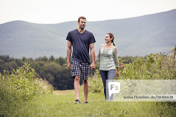 A couple  man and woman walking through a meadow holding hands.