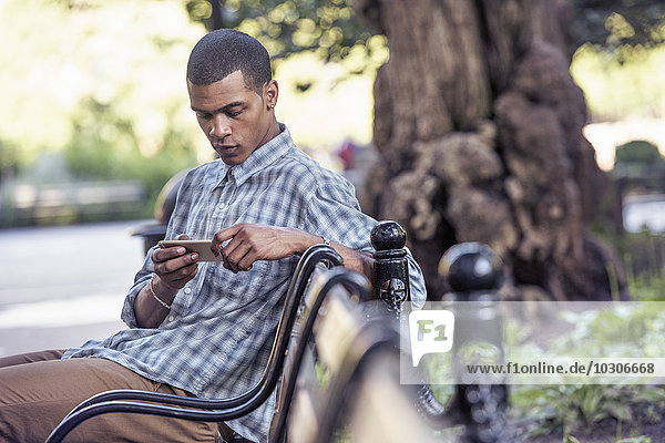 A man seated on a park bench using his smart phone