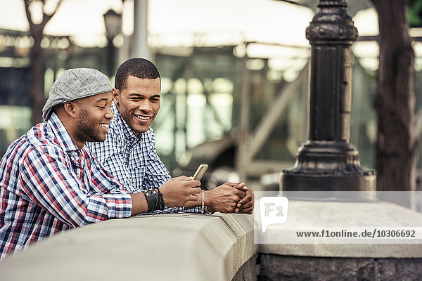 Two men side by side leaning on a parapet by a bridge looking at a smart phone