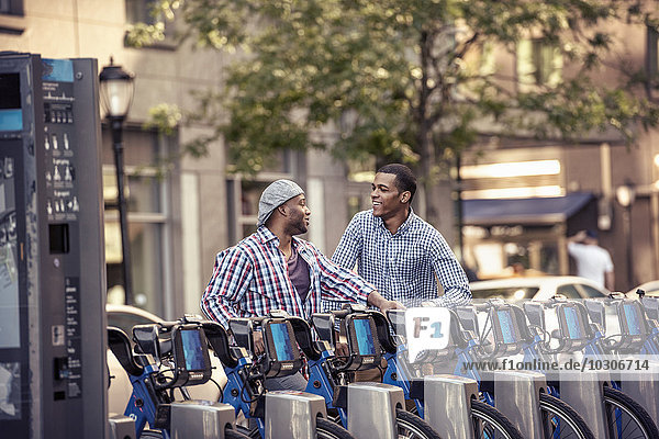 Two men by a rack of bicycles for hire in a city park