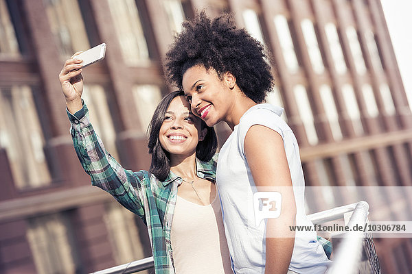 Zwei Frauen  die vor einem großen Gebäude in der Stadt posieren und ein Selfie machen