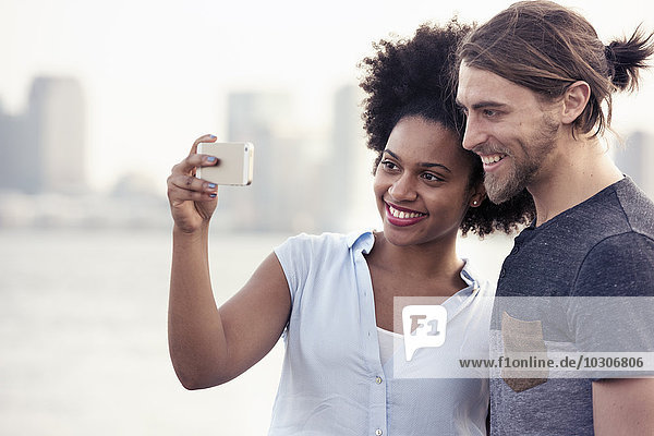 A couple  man and woman taking a selfie by the waterfront in a city