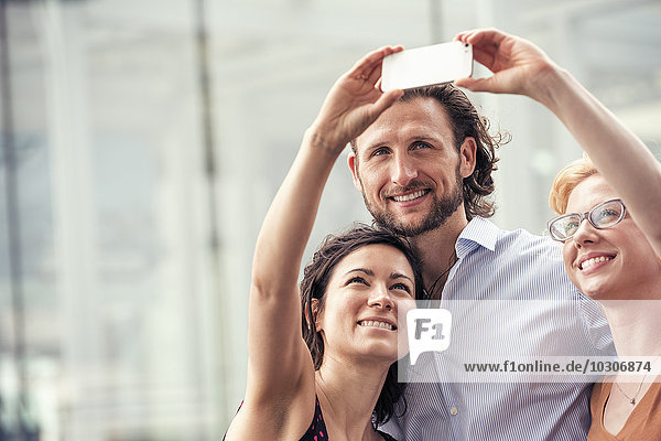 Ein Mann und zwei Frauen auf einer Straße in der Stadt  die mit einem Smartphone einen Selfie mitnehmen.
