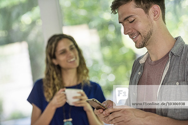 Ein Mann  der sein Telefon überprüft  und eine Frau  die eine Tasse Kaffee hält.