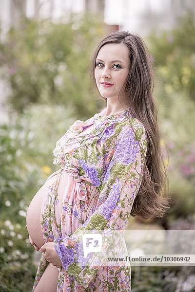 Porträt einer schwangeren Frau im modischen Bademantel  die ihren Bauch hält.
