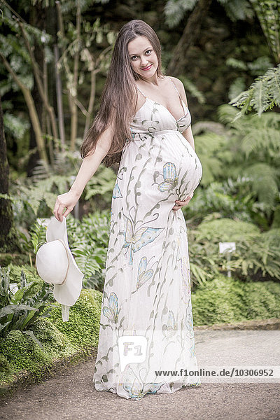 Porträt einer schwangeren Frau im Sommerkleid stehend im Gewächshaus