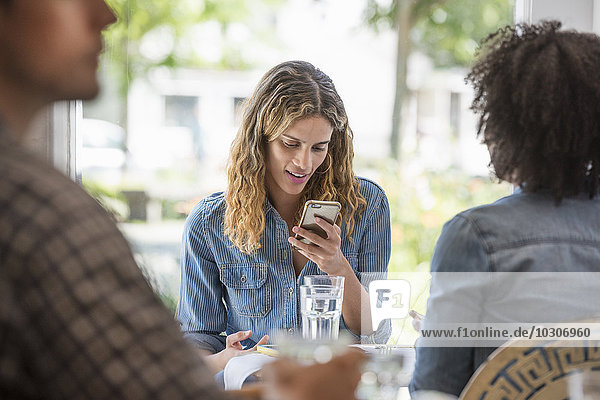 A woman looking at a smart phone seated with two other people in a cafe.