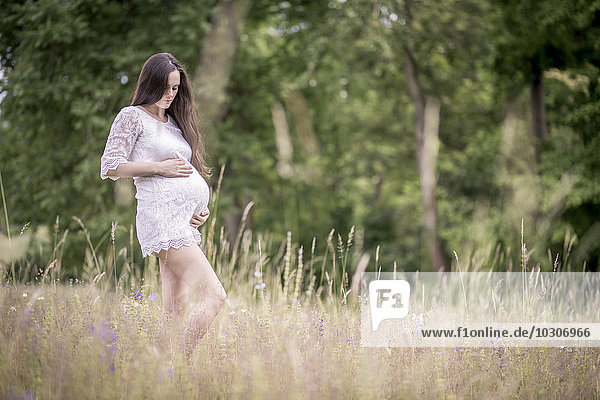 Schwangere Frau  die auf einer Wiese steht und ihren Bauch hält.