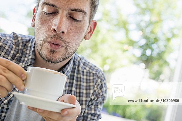 Ein Mann bläst auf die Oberfläche seines heißen Kaffees.