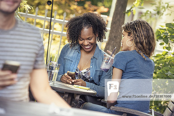 Drei Personen in einem Café-Restaurant  zwei überprüfen ihre Smartphones