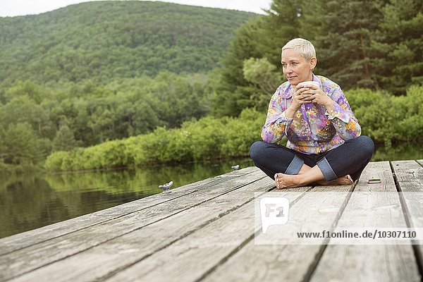 A woman sitting outdoors on a dock with a cup of coffee