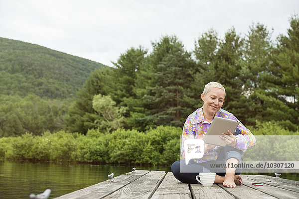 A woman sitting outdoors on a jetty using a digital tablet.