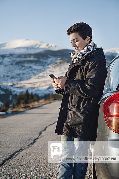 Teenage boy leaning on car  using smart phone