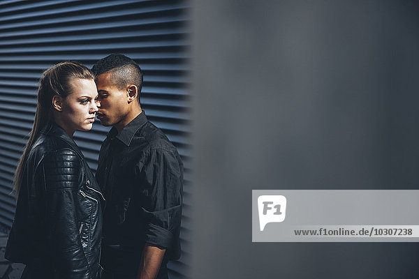 Schwarz gekleidetes junges Paar vor schwarzer Fassade stehend