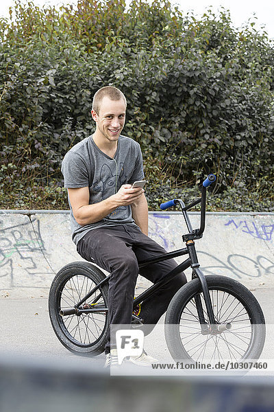 Junger Mann mit Smartphone sitzend auf BMX-Bike