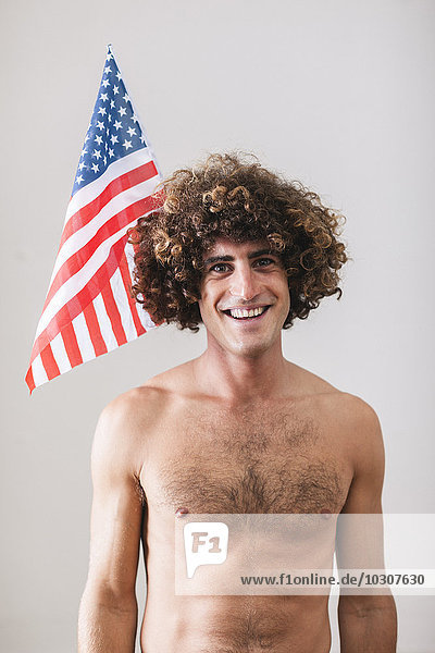 Porträt eines nackten Mannes mit lockigen Haaren vor der amerikanischen Flagge