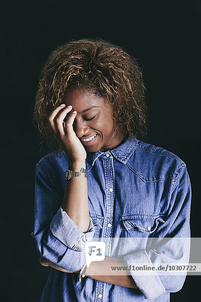 Portrait of smiling woman with closed eyes and hand on her face in front of black background