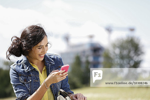 Deutschland  Berlin  Portrait einer glücklichen jungen Frau mit ihrem Smartphone