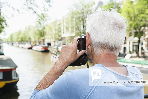 Niederlande  Amsterdam  älterer Mann beim Fotografieren mit analoger Kamera am Stadtkanal