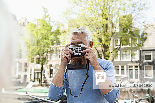 Netherlands  Amsterdam  senior man taking a picture with analog camera